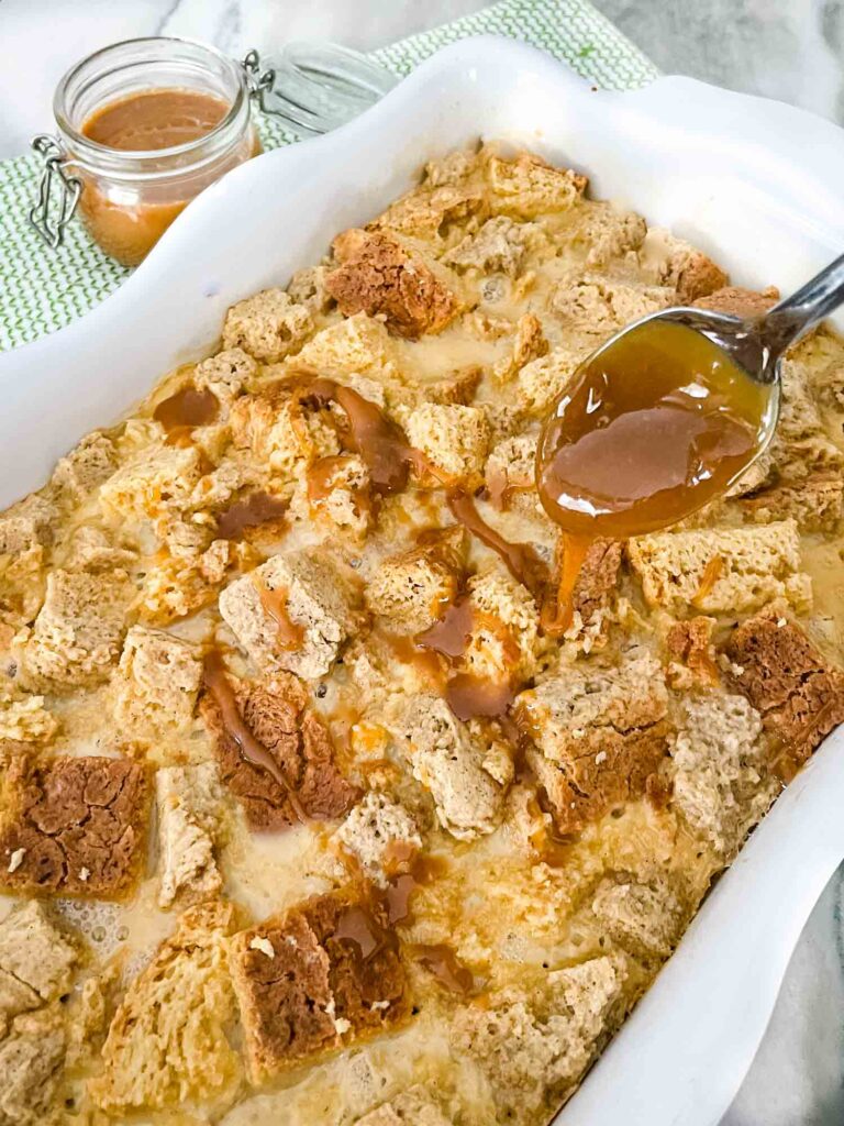 A spoon pouring Bailey's Dessert sauce over a full dish of Irish Cream Bread Pudding