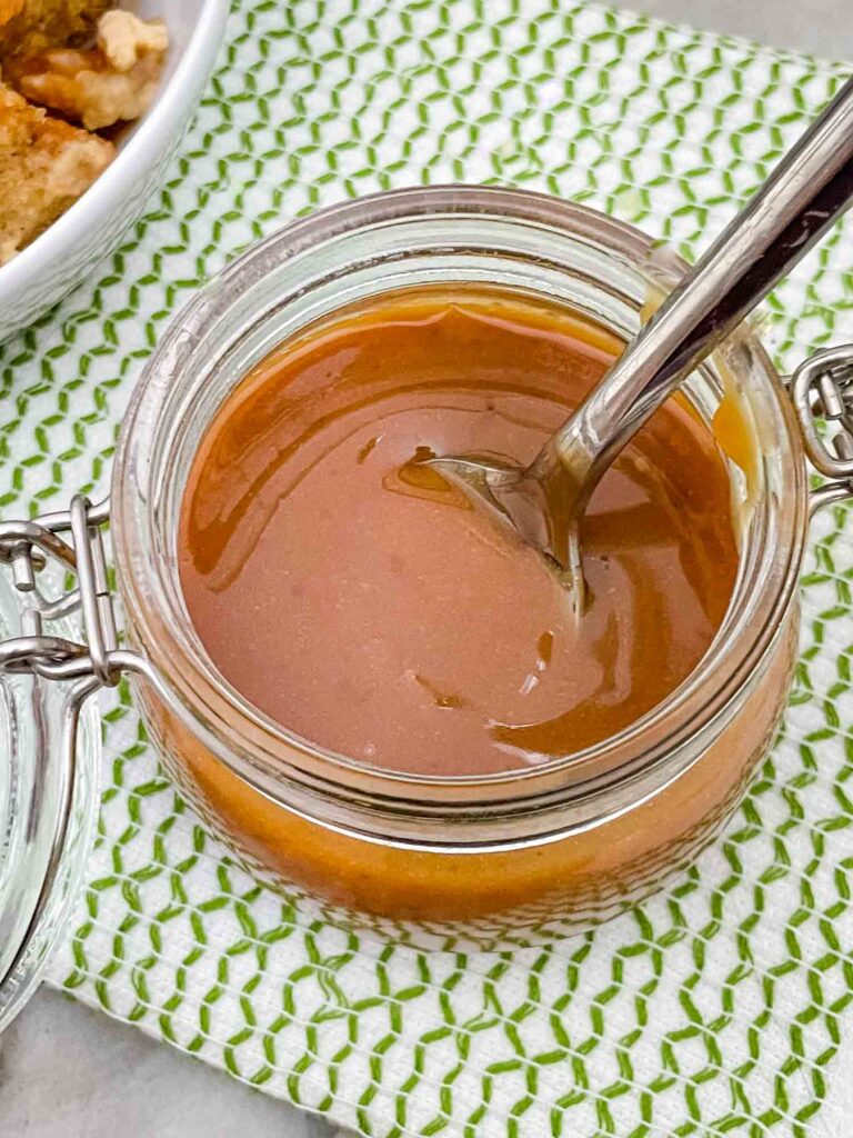 Top view of Irish Cream Dessert Sauce in a small jar on a green and white towel with a silver spoon in it