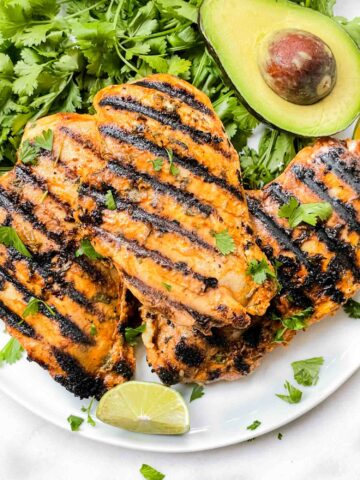 Cilantro Lime Grilled Chicken breasts on a plate with cilantro and avocado around it