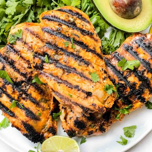 Cilantro Lime Grilled Chicken breasts on a plate with cilantro and avocado around it