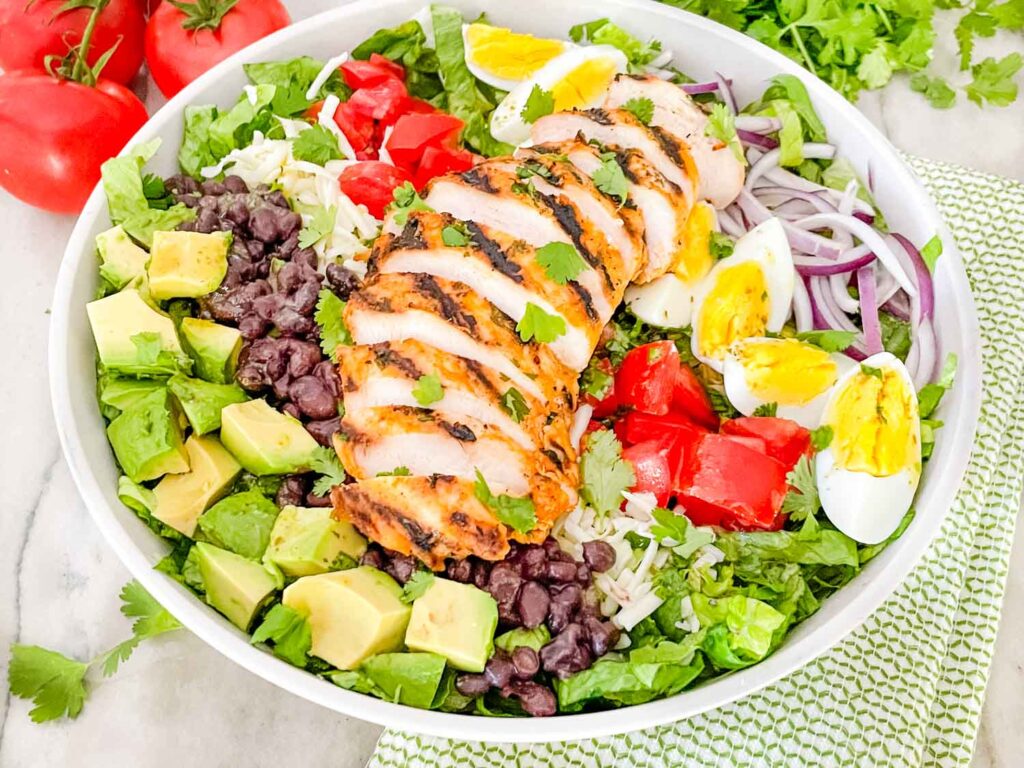A bowl of Mexican Cobb Salad with sliced chicken on top sitting on a counter