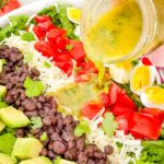 A hand pouring cilantro lime vinaigrette dressing on top of a Mexican Cobb Salad