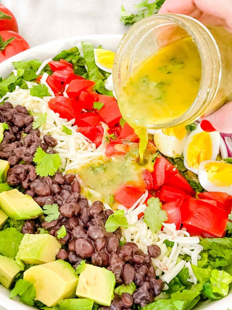 A hand pouring cilantro lime vinaigrette dressing on top of a Mexican Cobb Salad