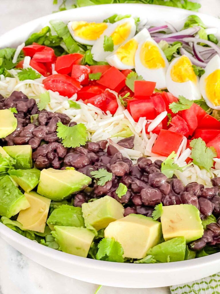 Mexican Cobb Salad with avocado, black beans, tomato, cheese, egg, and onion on top of lettuce in rows