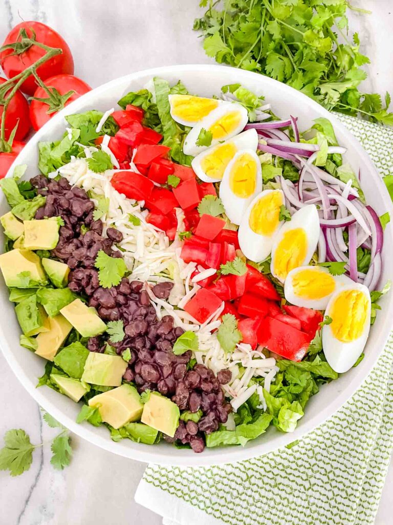 Top view of Mexican Cobb Salad on a counter with the toppings in rows on top of the lettuce