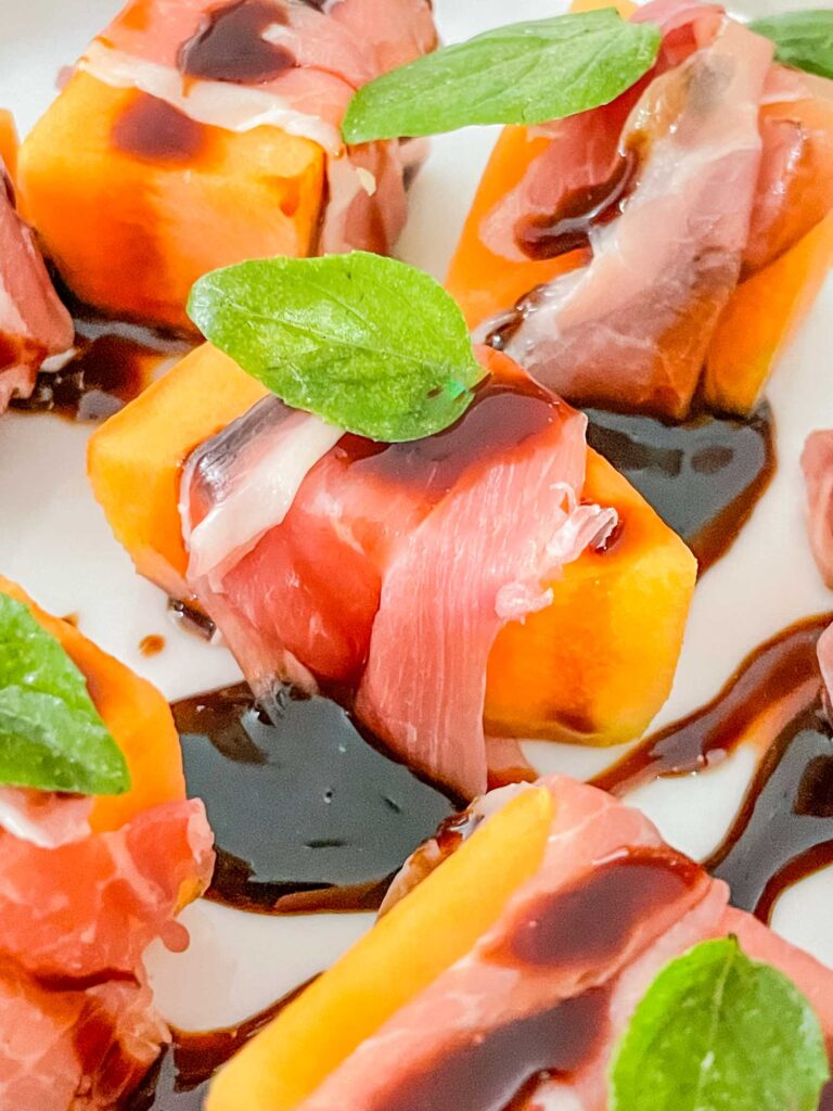 A close view of one piece of Prosciutto Wrapped Melon with Balsamic Glaze