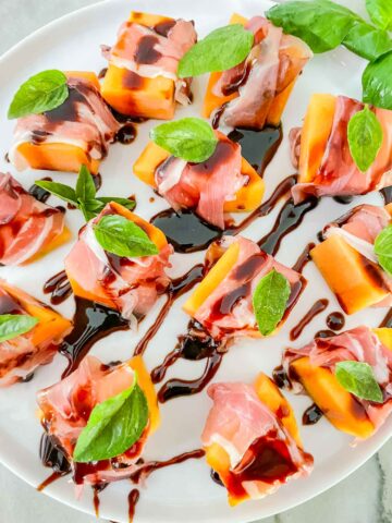 A white plate full of Prosciutto Wrapped Melon with Balsamic Glaze pieces