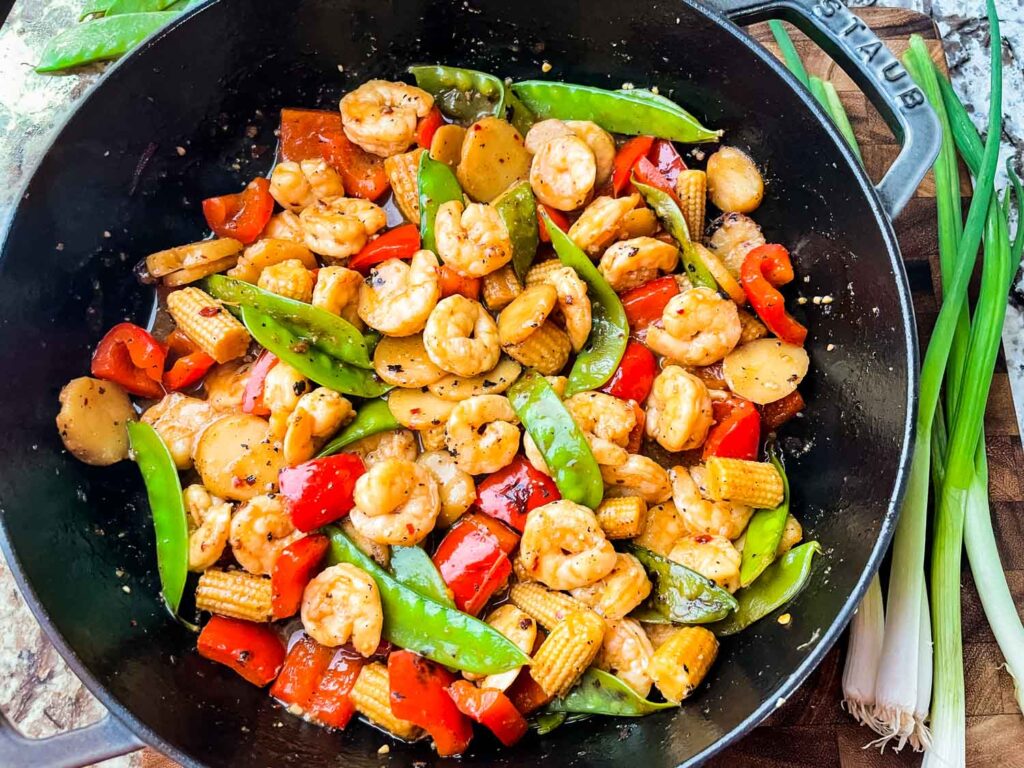 Top view of Sweet and Sour Shrimp Stir Fry in a large wok with green onions next to it