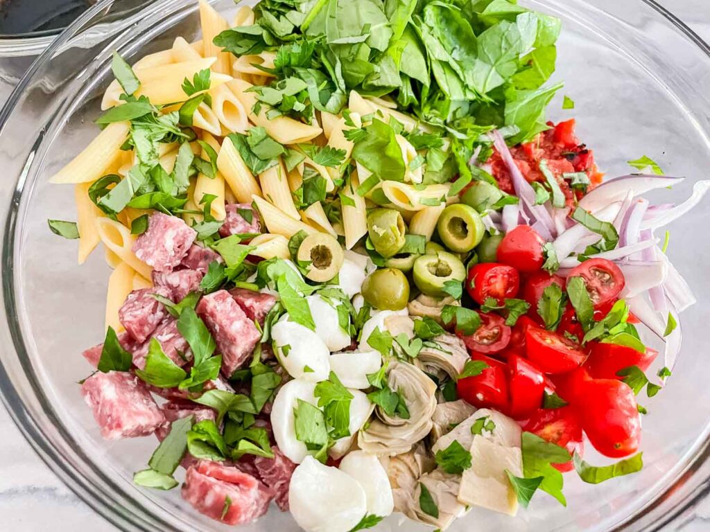 The ingredients for the pasta salad separated in a glass bowl