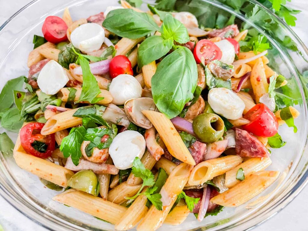 Italian Antipasto Pasta Salad in a glass bowl with a basil sprig garnish