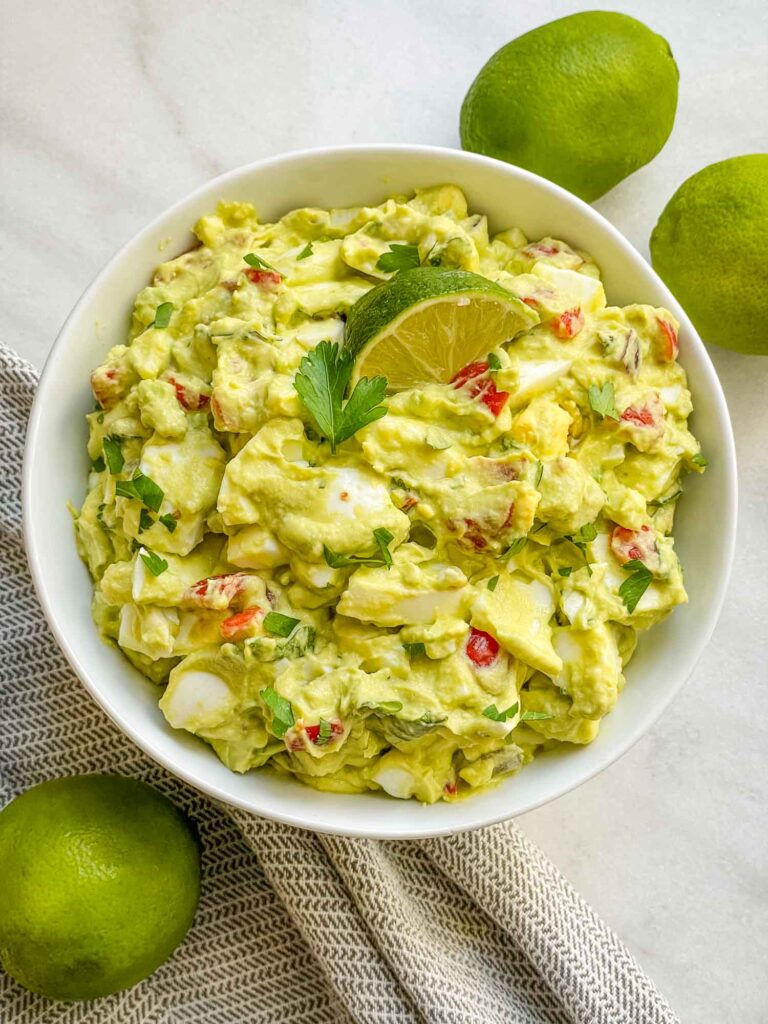 Looking down on a bowl full of Avocado Egg Salad on a counter with limes around it