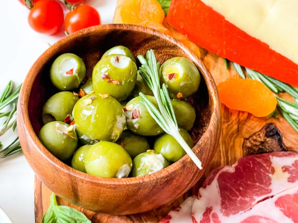 A small wood bowl full of Blue Cheese Stuffed Olives sitting on a charcuterie board