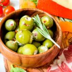 A wood bowl full of Blue Cheese Stuffed Olives sitting on a charcuterie board