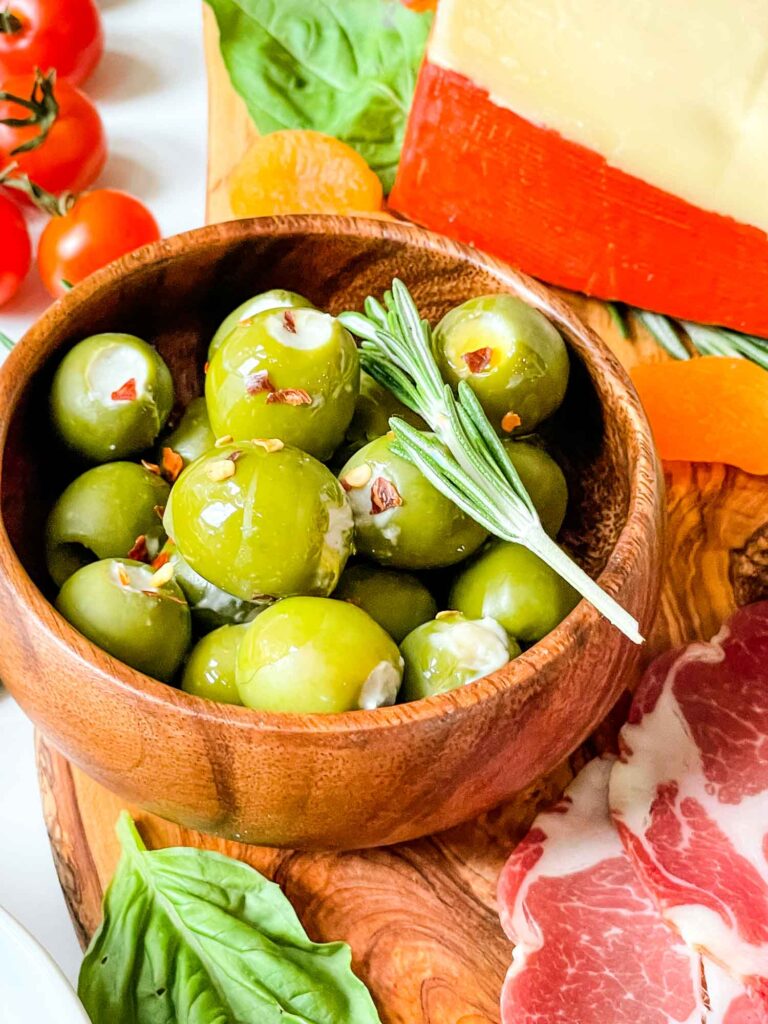 A wood bowl full of Blue Cheese Stuffed Olives sitting on a charcuterie board
