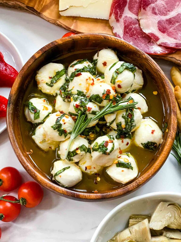 Top view of Marinated Mozzarella Balls in a wood bowl surrounded by meats