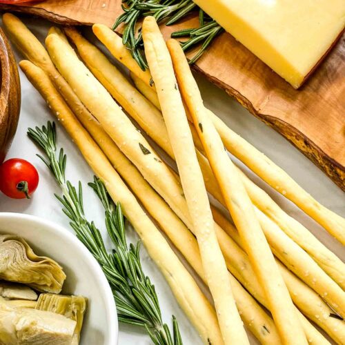 A pile of Rosemary Grissini Italian breadsticks surrounded by charcuterie