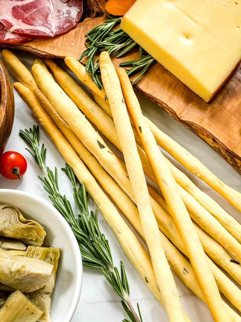 A pile of Rosemary Grissini Italian breadsticks surrounded by charcuterie