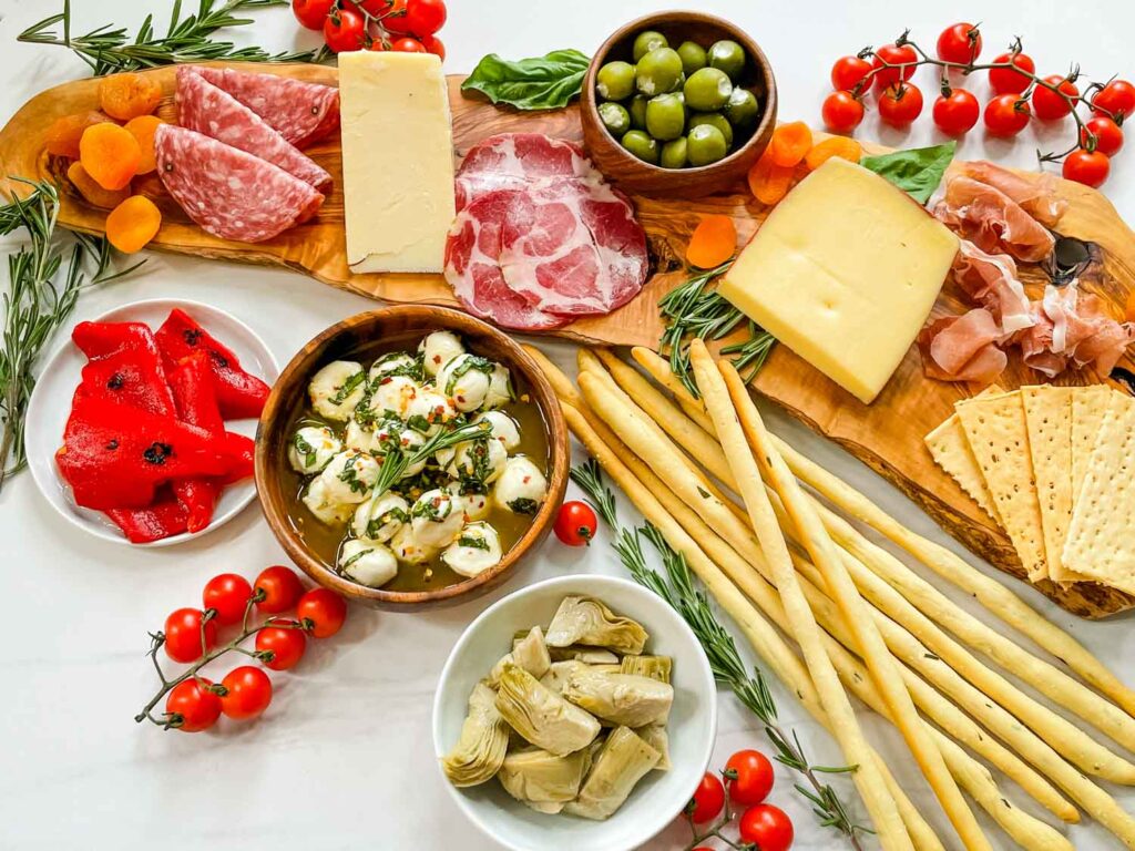 Antipasti Italian Charcuterie Board on a white counter. A wood board loaded with meats, cheese, olives, and other foods.