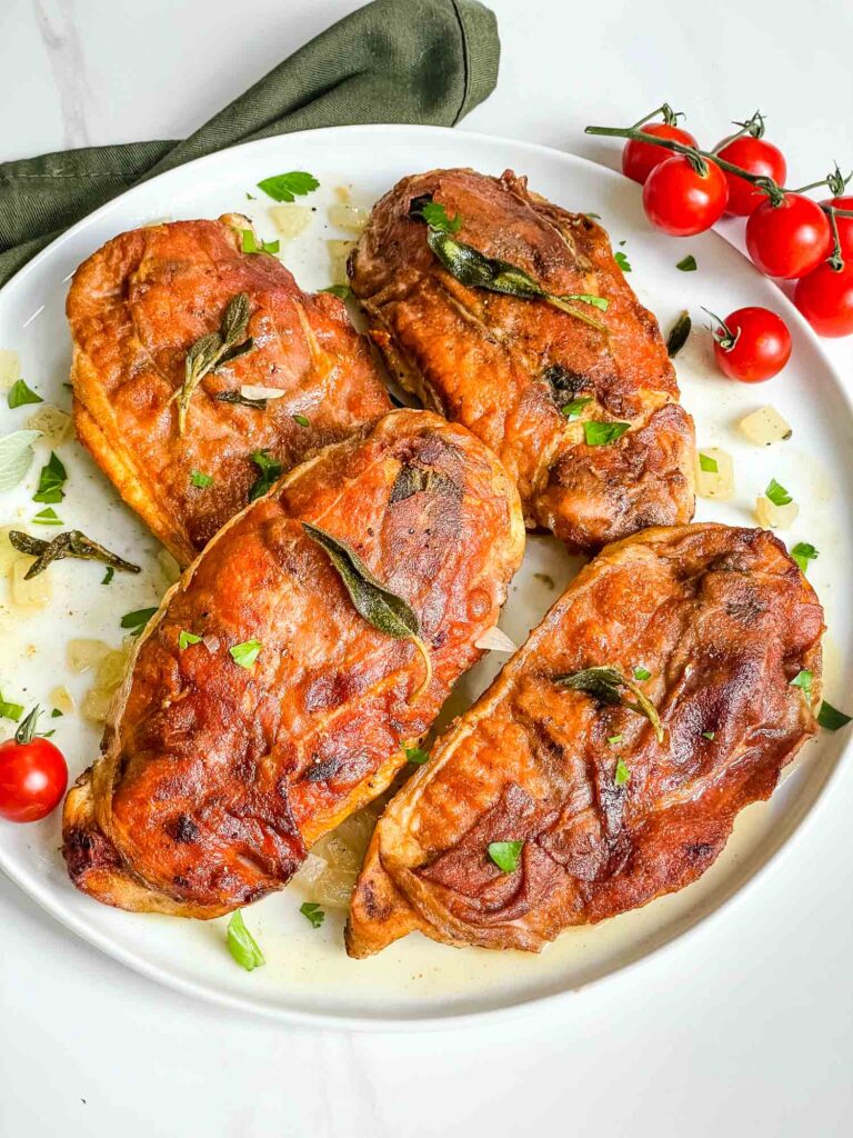 A white plate full of four Chicken Saltimbocca alla Romana pieces on a counter.