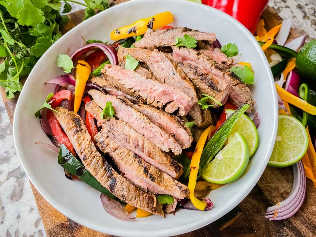 Looking down on Chipotle Steak Fajitas in a white bowl sitting on a wood board