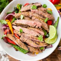 Top view of Chipotle Steak Fajitas in a white bowl with the peppers and onions, sitting on a cutting board