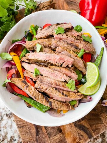 Top view of Chipotle Steak Fajitas in a white bowl with the peppers and onions, sitting on a cutting board