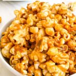 Pin of Homemade Caramel Popcorn Recipe (without Corn Syrup) in a white bowl up close with title at top.