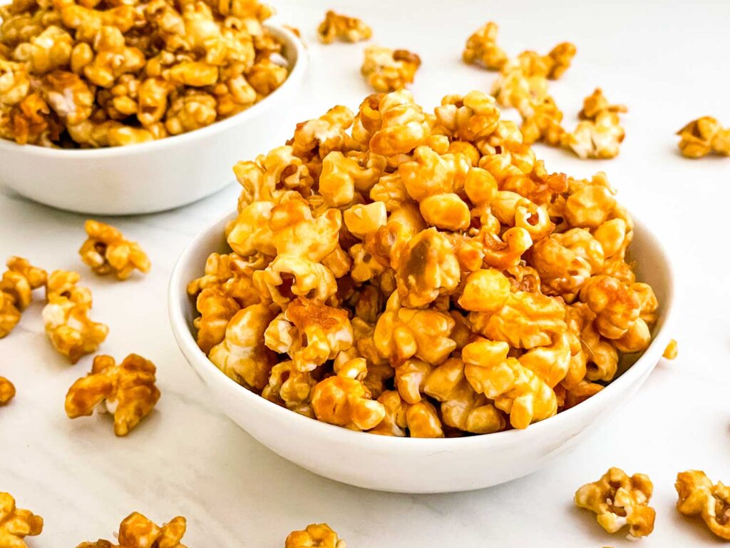 A small white bowl full of Homemade Caramel Popcorn Recipe (without Corn Syrup) on a counter.