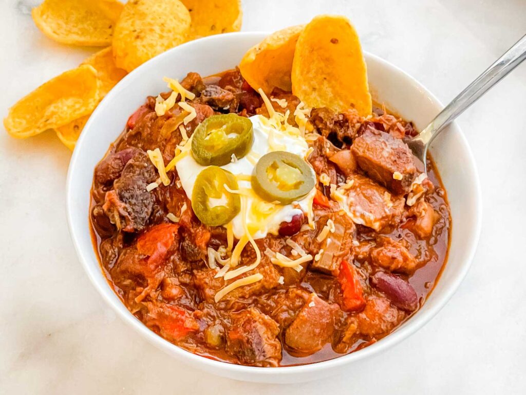 Smoked Brisket Chili Recipe in a white bowl on a counter with toppings.