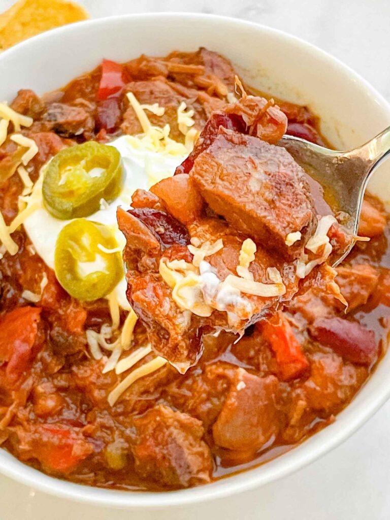 A spoon scooping some Smoked Brisket Chili Recipe out of a bowl.