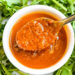 A spoon scooping some Sundried Tomato Vinaigrette Salad Dressing out of a white dish surrounded by lettuce.