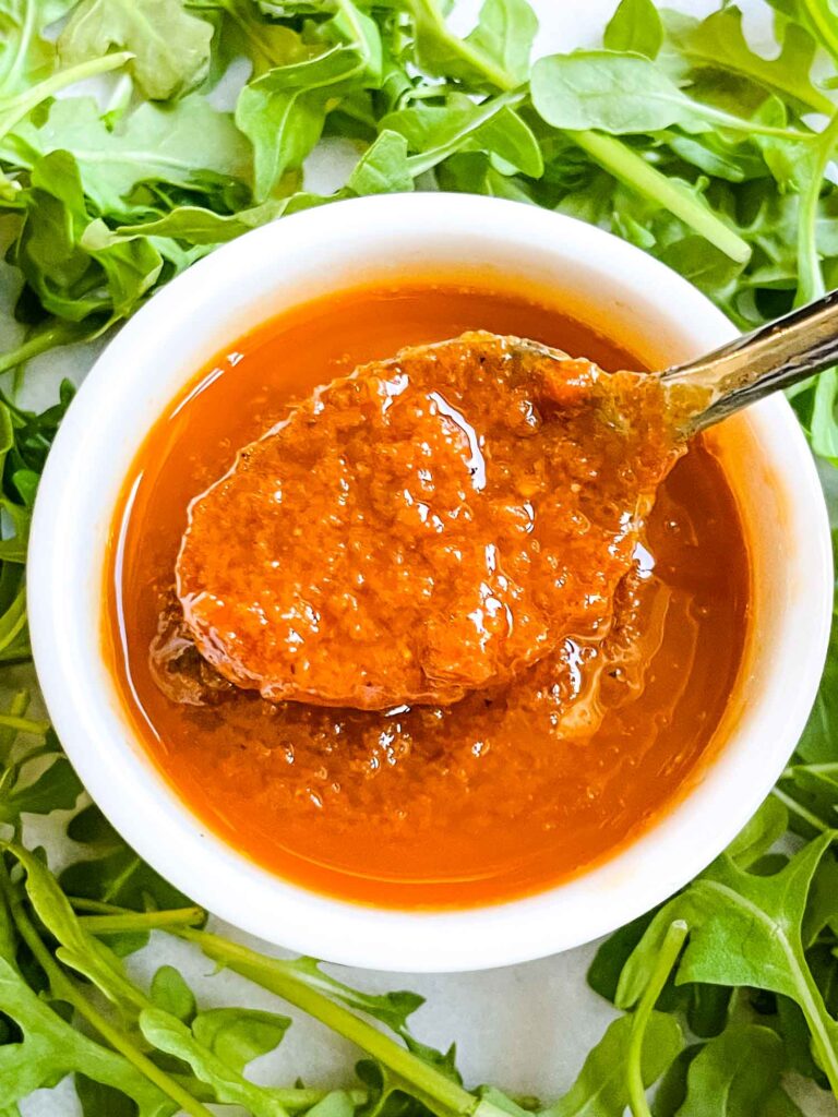 A spoon scooping some Sundried Tomato Vinaigrette Salad Dressing out of a white dish surrounded by lettuce.