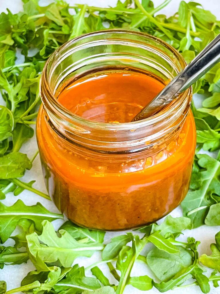 Sundried Tomato Vinaigrette Salad Dressing in a small glass jar surrounded by arugula.