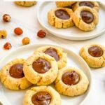 Pin of Chocolate Hazelnut Thumbprint Cookies on a small plate on a counter with title at top.