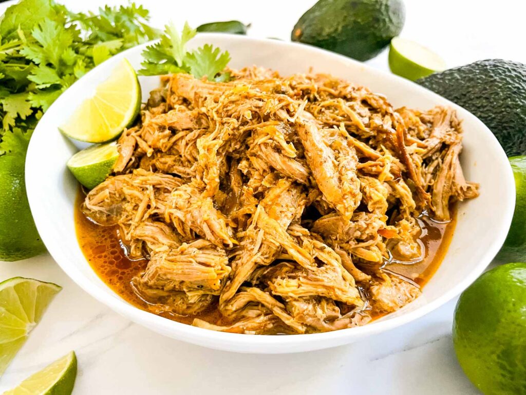 Shredded Instant Pot Pork Carnitas in a white bowl on a counter.