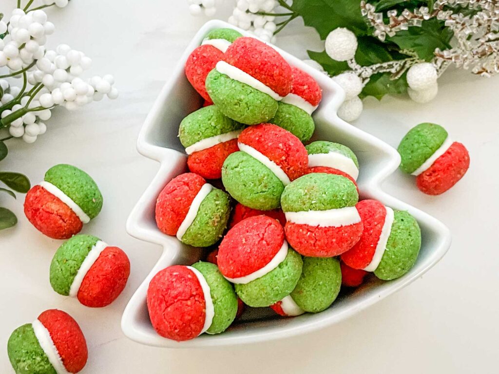 Red, white, and green Christmas Baci di Dama Cookies in a tree shaped bowl on a counter.