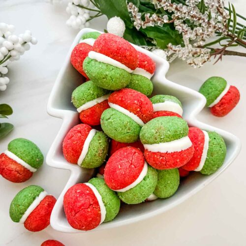 Red and green Christmas Baci di Dama Cookies in a tree shaped bowl on a counter.