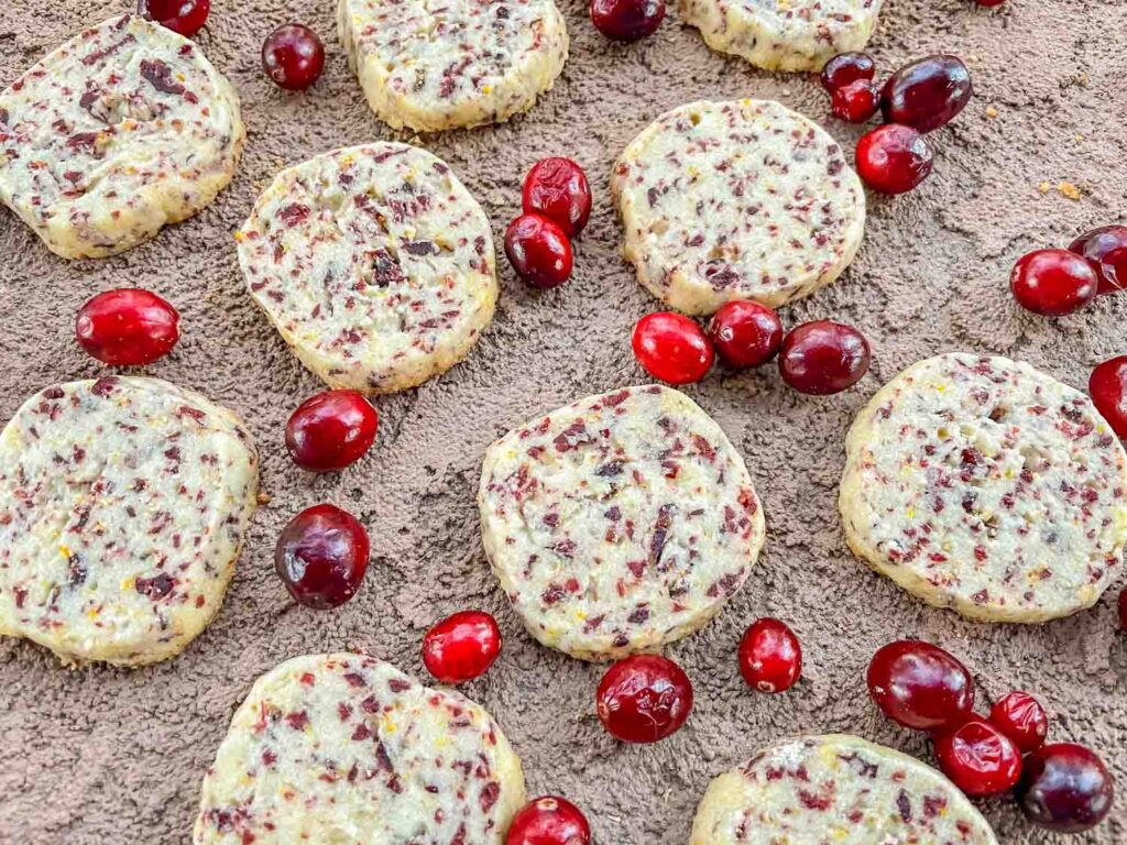 Cranberry Orange Shortbread Cookies scattered on a stone surface with fresh cranberries.