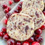 Closer view of round Cranberry Orange Shortbread Cookies on a bed of fresh cranberries in a row.