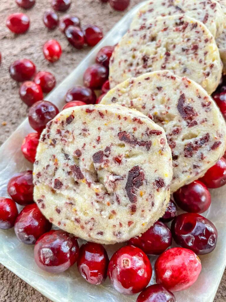 Closer view of round Cranberry Orange Shortbread Cookies on a bed of fresh cranberries in a row.