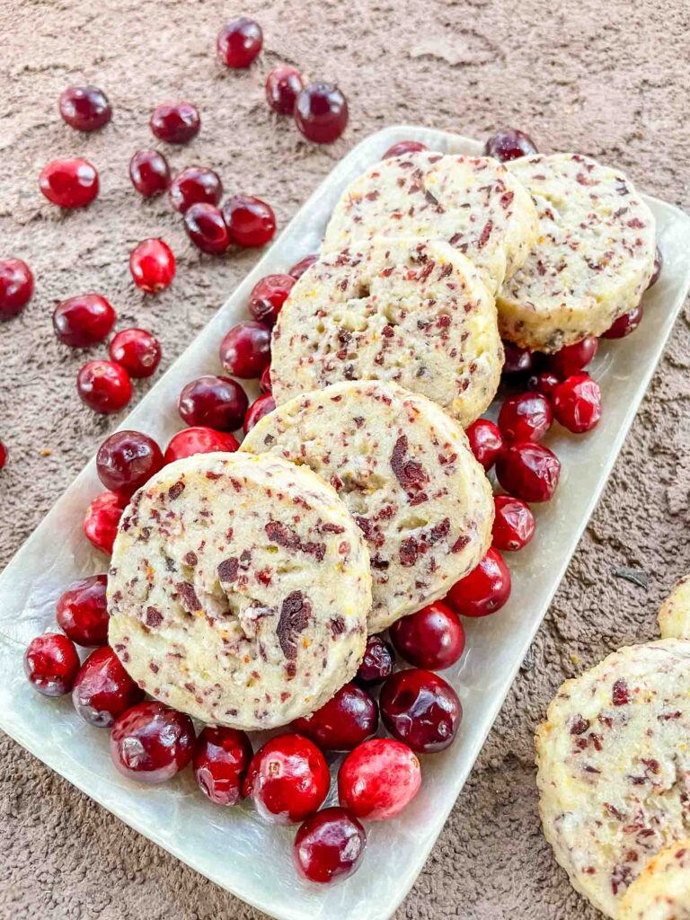 Cranberry Orange Shortbread Cookies on a bed of fresh cranberries in a rectangular tray on a stone surface.