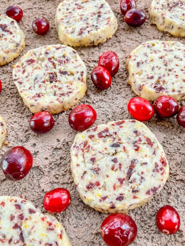 Closer view of Cranberry Orange Shortbread Cookies scattered on a stone surface with fresh cranberries.