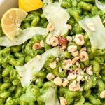 Close view of Hazelnut Spinach Pesto Cavatappi garnished with chopped nuts, lemon wedges, and cheese shards.