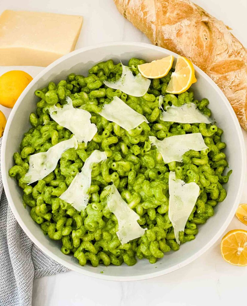 Looking down on a bowl of Hazelnut Spinach Pesto Cavatappi on a counter surrounded by ingredients.