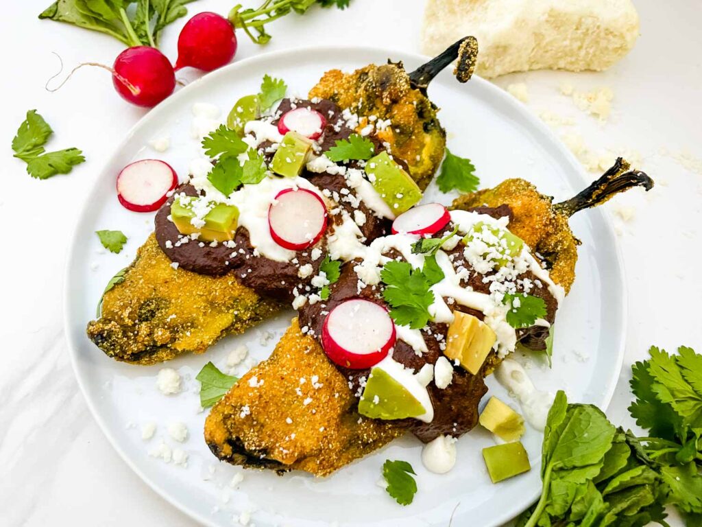 Two Mole Chile Rellenos on a white plate on a counter.