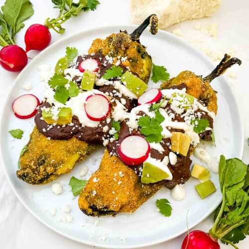 Two Mole Chile Rellenos on a white plate with radish, cilantro, and sour cream garnishes.