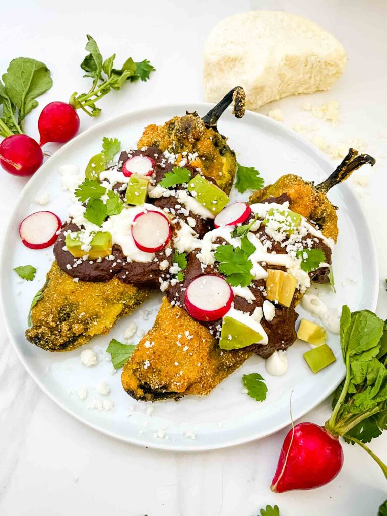Two Mole Chile Rellenos on a white plate with radish, cilantro, and sour cream garnishes.