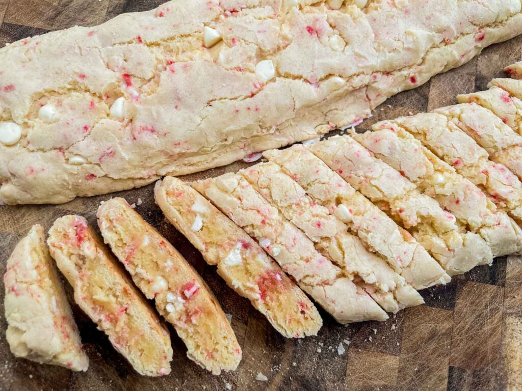 Slicing the White Chocolate Peppermint Biscotti logs into the cookie slices on a cutting board.