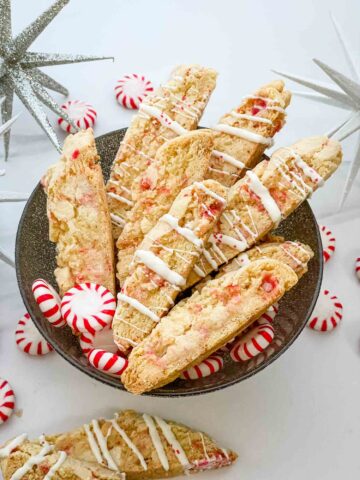 White Chocolate Peppermint Biscotti cookies in a bowl on a counter with peppermints around it.