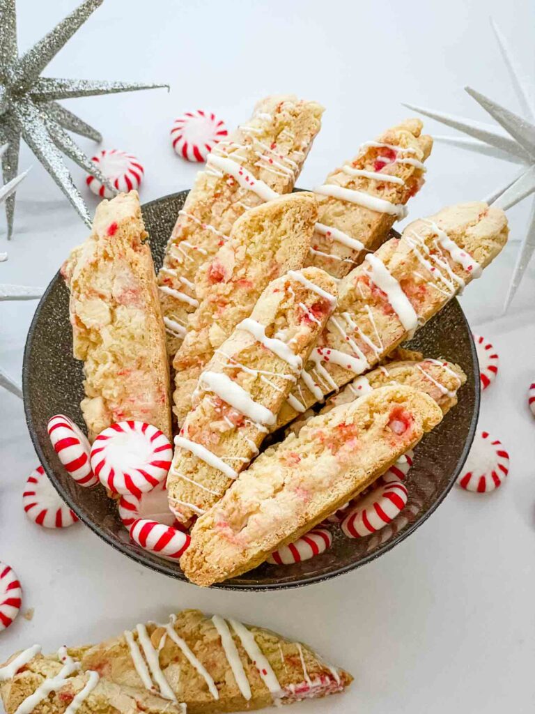 White Chocolate Peppermint Biscotti cookies in a bowl on a counter with peppermints around it.